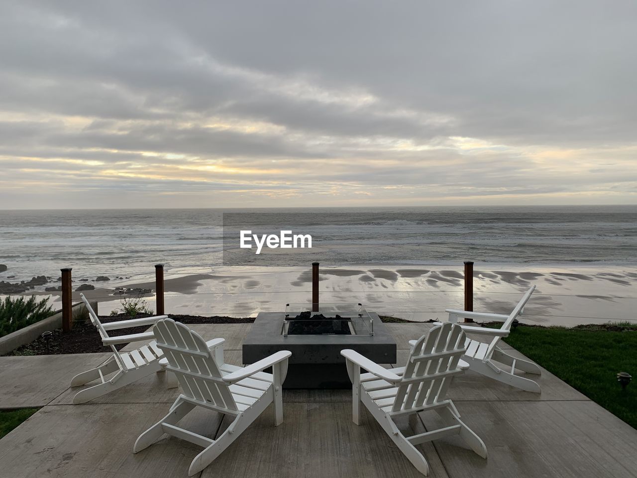 EMPTY CHAIRS AND TABLES ON BEACH AGAINST SKY