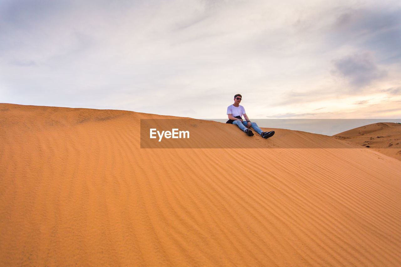 Man on sand dune at desert against sky