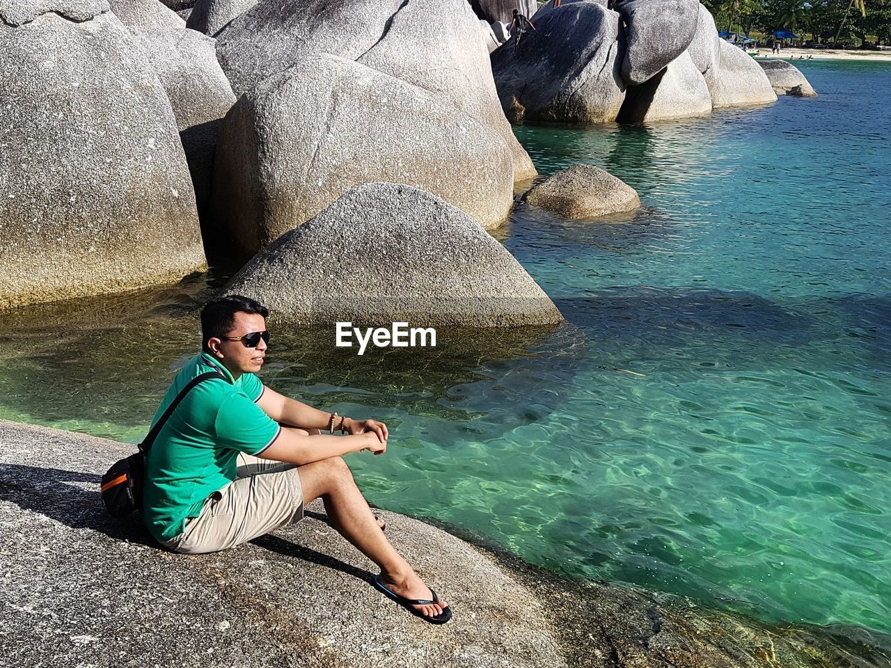 Full length of man sitting on rock by sea at belitung island during sunny day