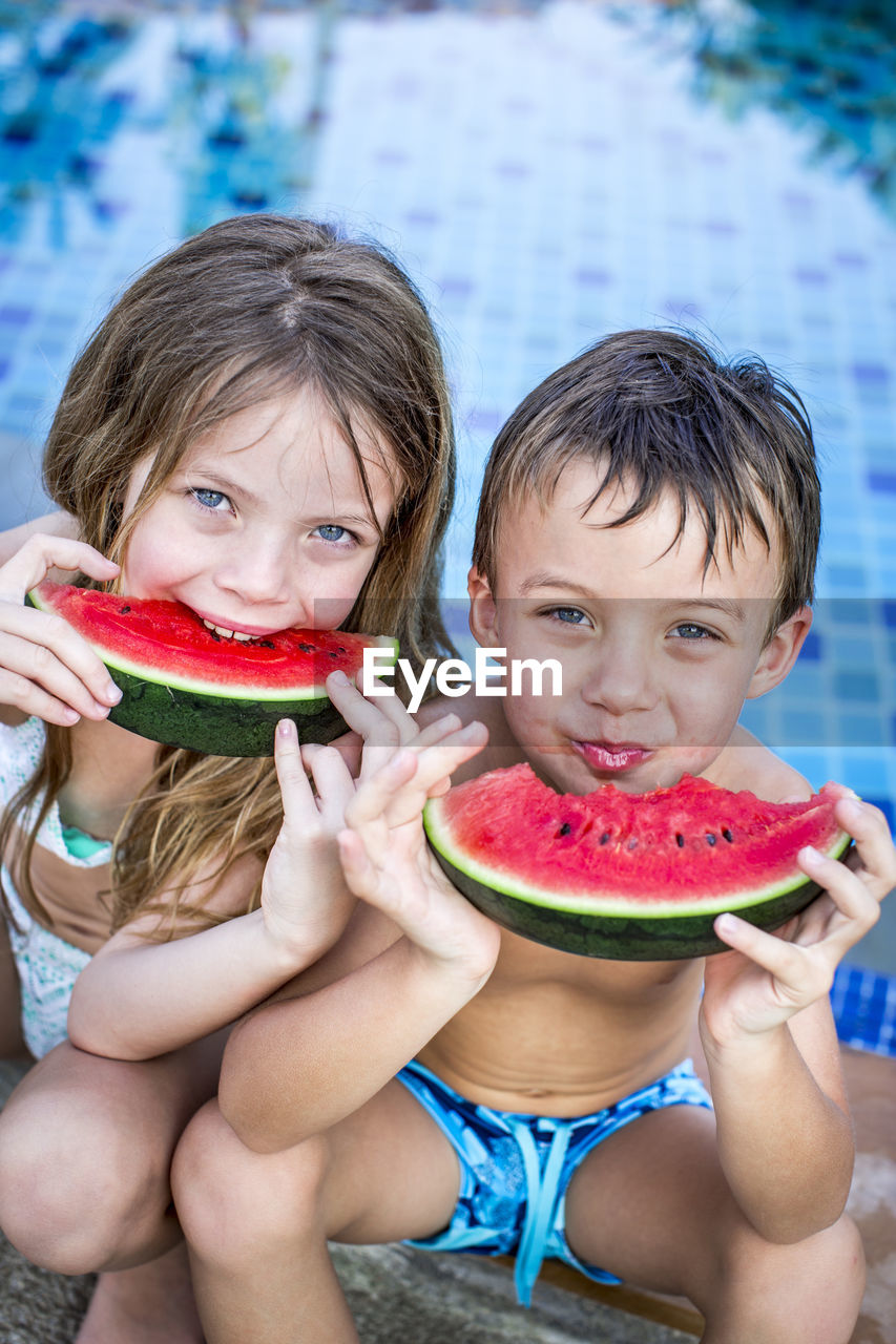 Cute siblings having watermelon against swimming pool