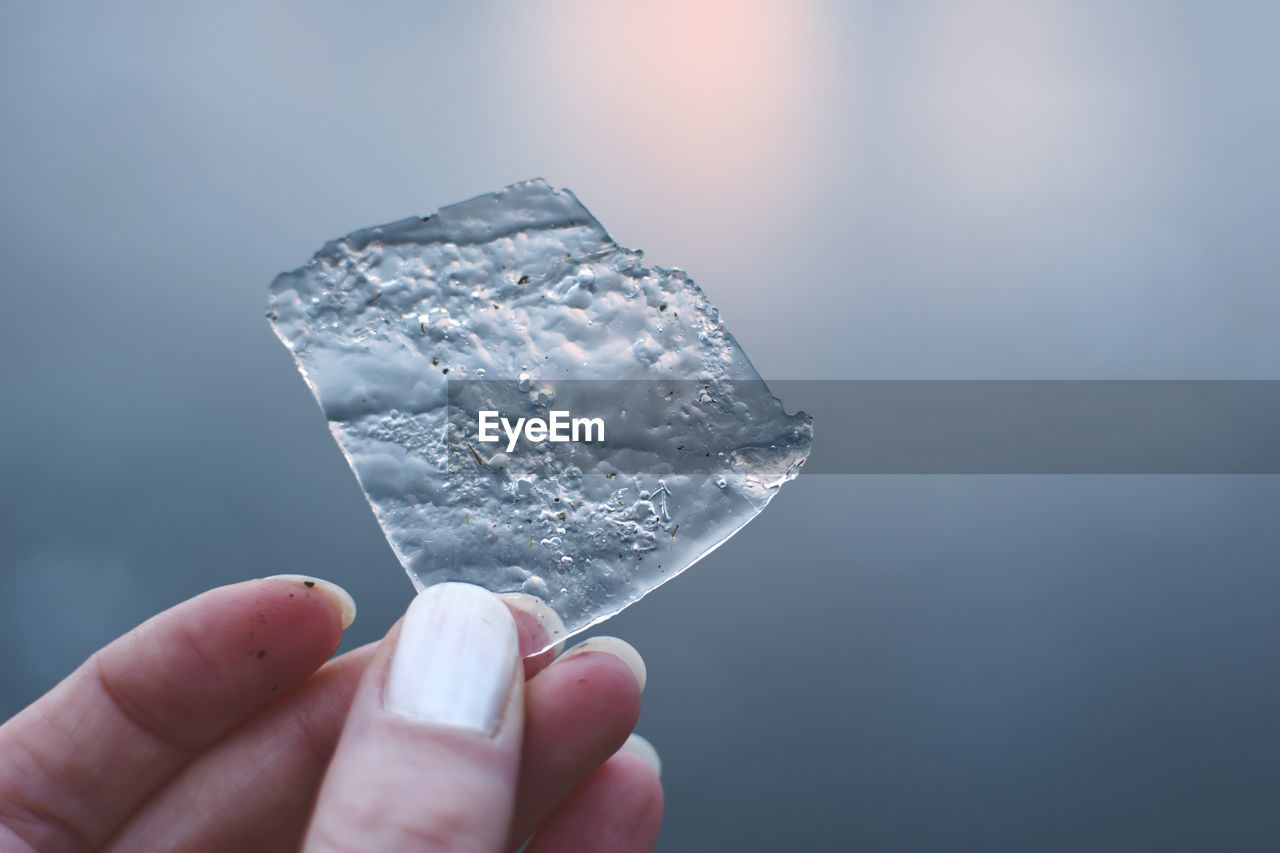 CLOSE-UP OF HAND HOLDING ICE CREAM OVER WATER AGAINST GRAY BACKGROUND