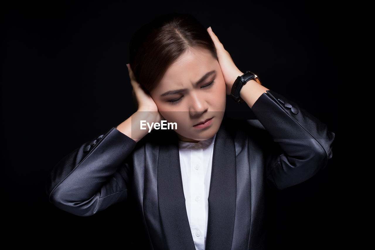 Businesswoman with hands covering ears against black background