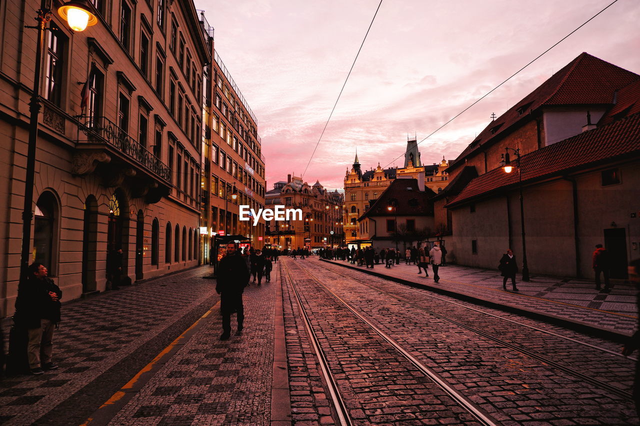 People walking on railroad tracks amidst buildings in city