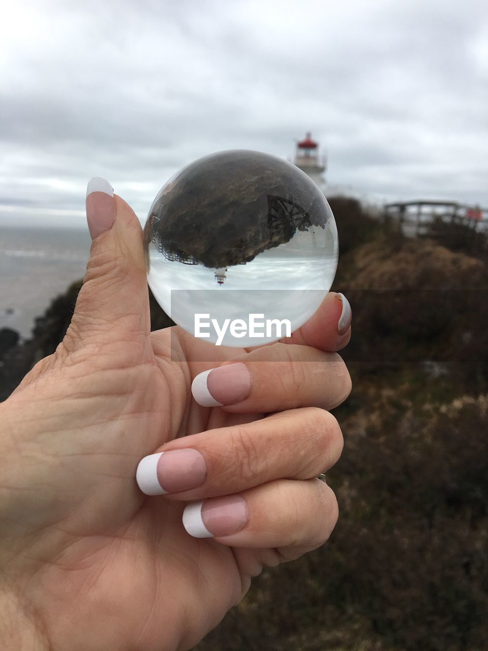 Cropped hand of woman holding crystal ball with reflection against lighthouse