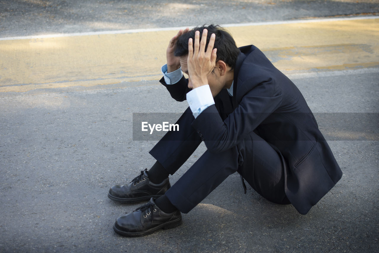 Side view of mid adult man with head in hands sitting on road