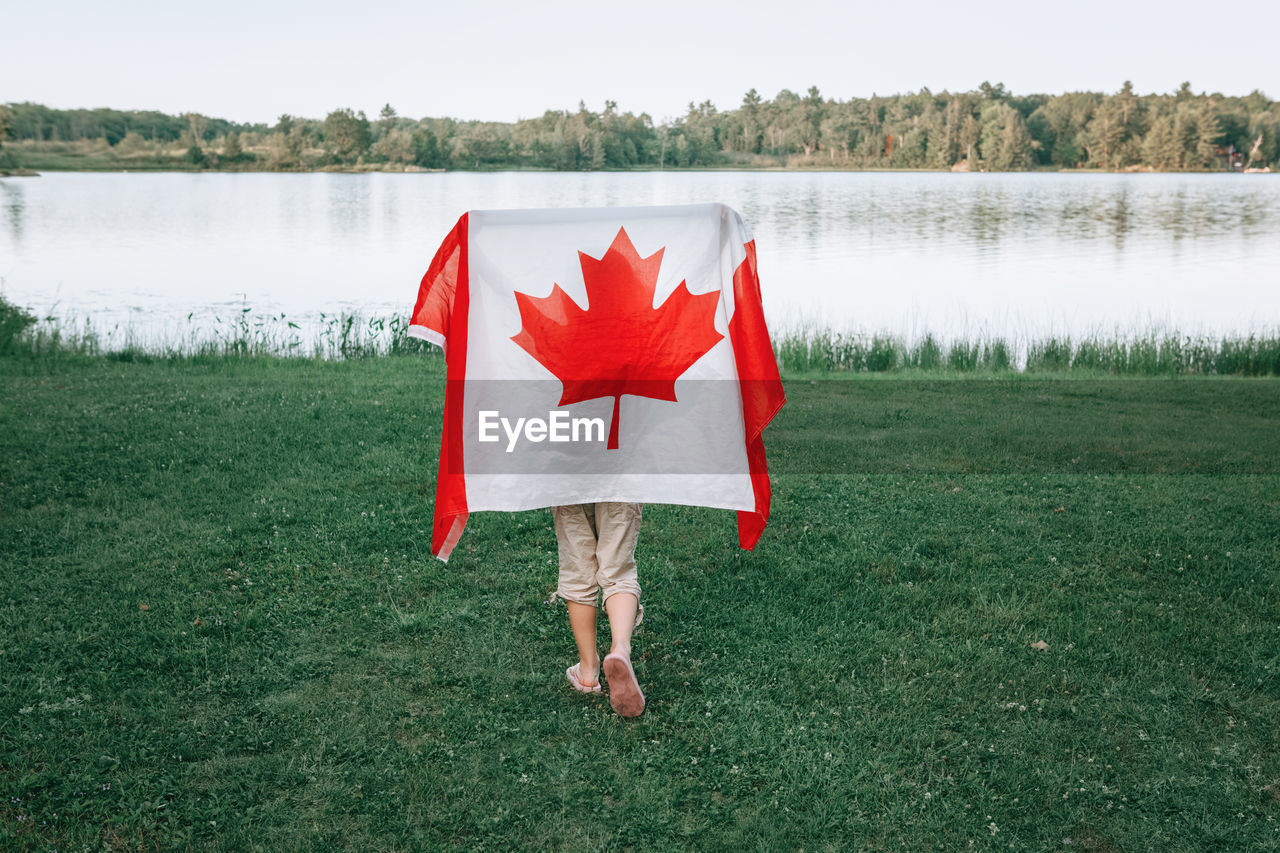 Rear view of girl holding canadian flag against lake