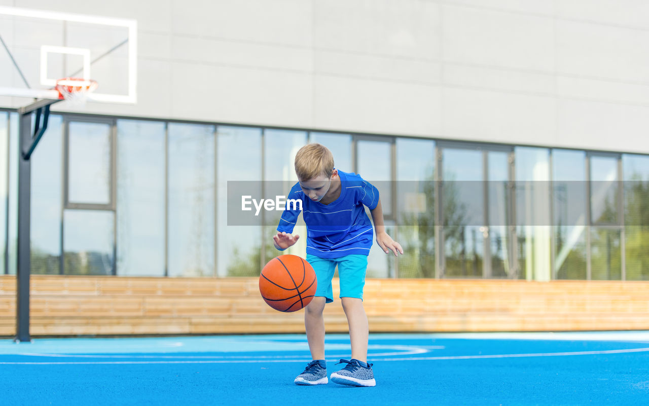 Boy playing with basketball while standing on sports court