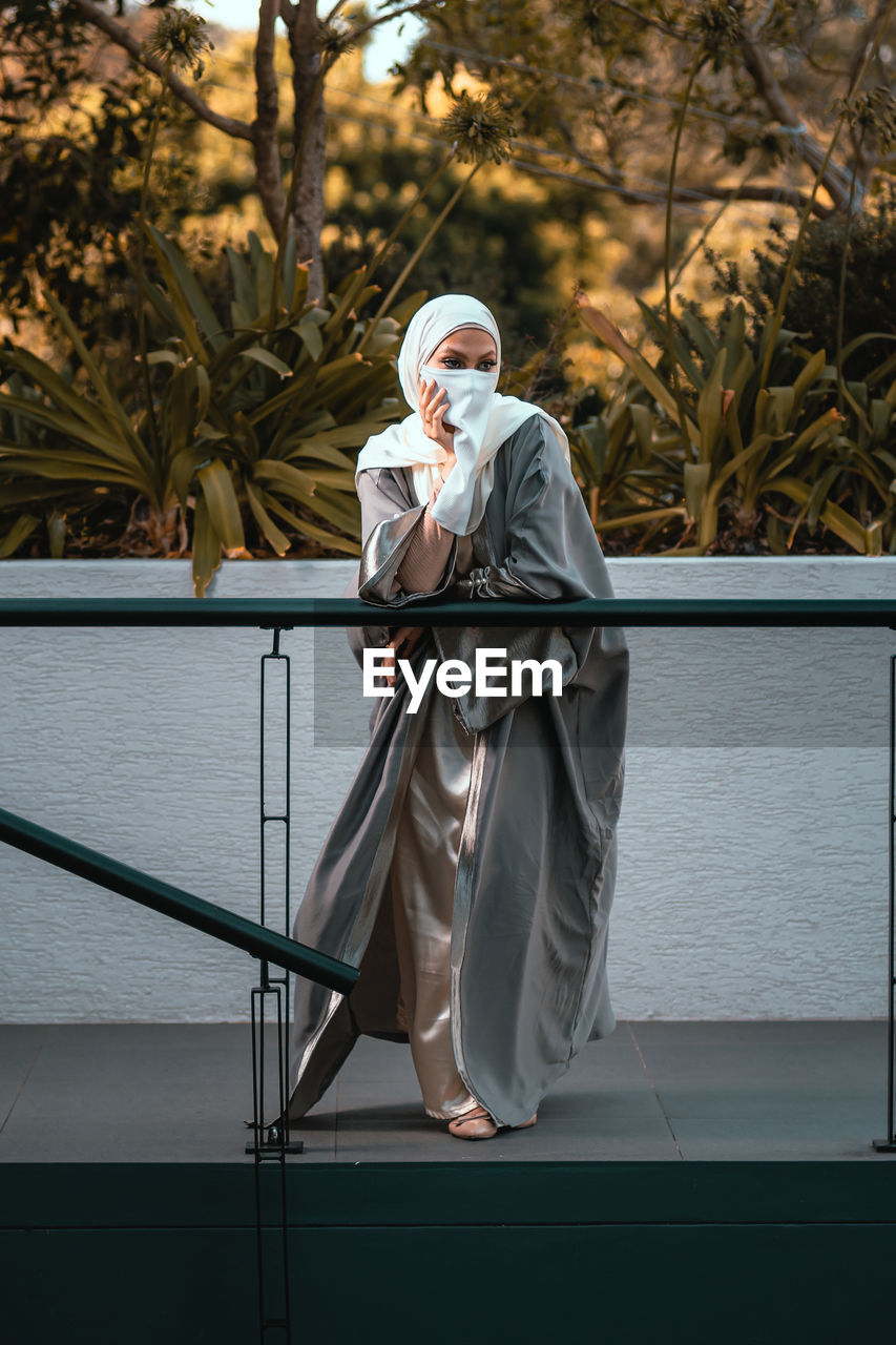 Full length picture of veiled woman with white niqab and hijab standing by railing