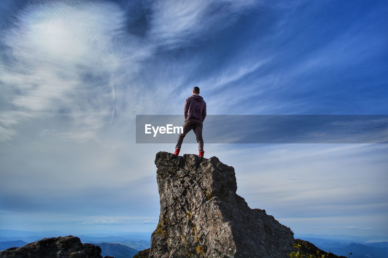 Low angle view of man standing on rock against sky