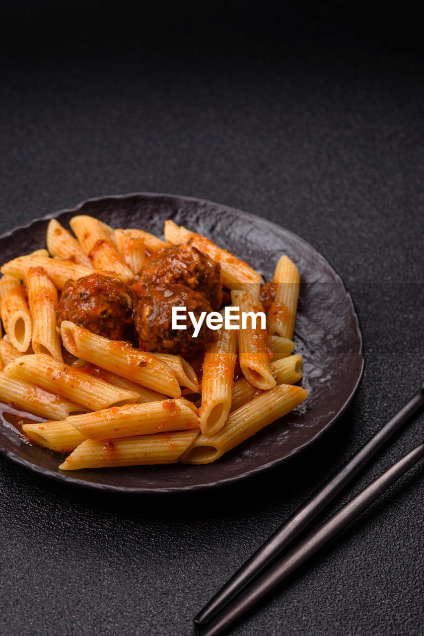 food, food and drink, studio shot, dish, fast food, cuisine, freshness, pasta, indoors, italian food, black background, no people, produce, fried, still life, plate, kitchen utensil, unhealthy eating, penne, meal, savory food, french fries, copy space, spaghetti, high angle view, dark, eating utensil, raw potato, condiment, wellbeing, gray background, close-up, fork, meat