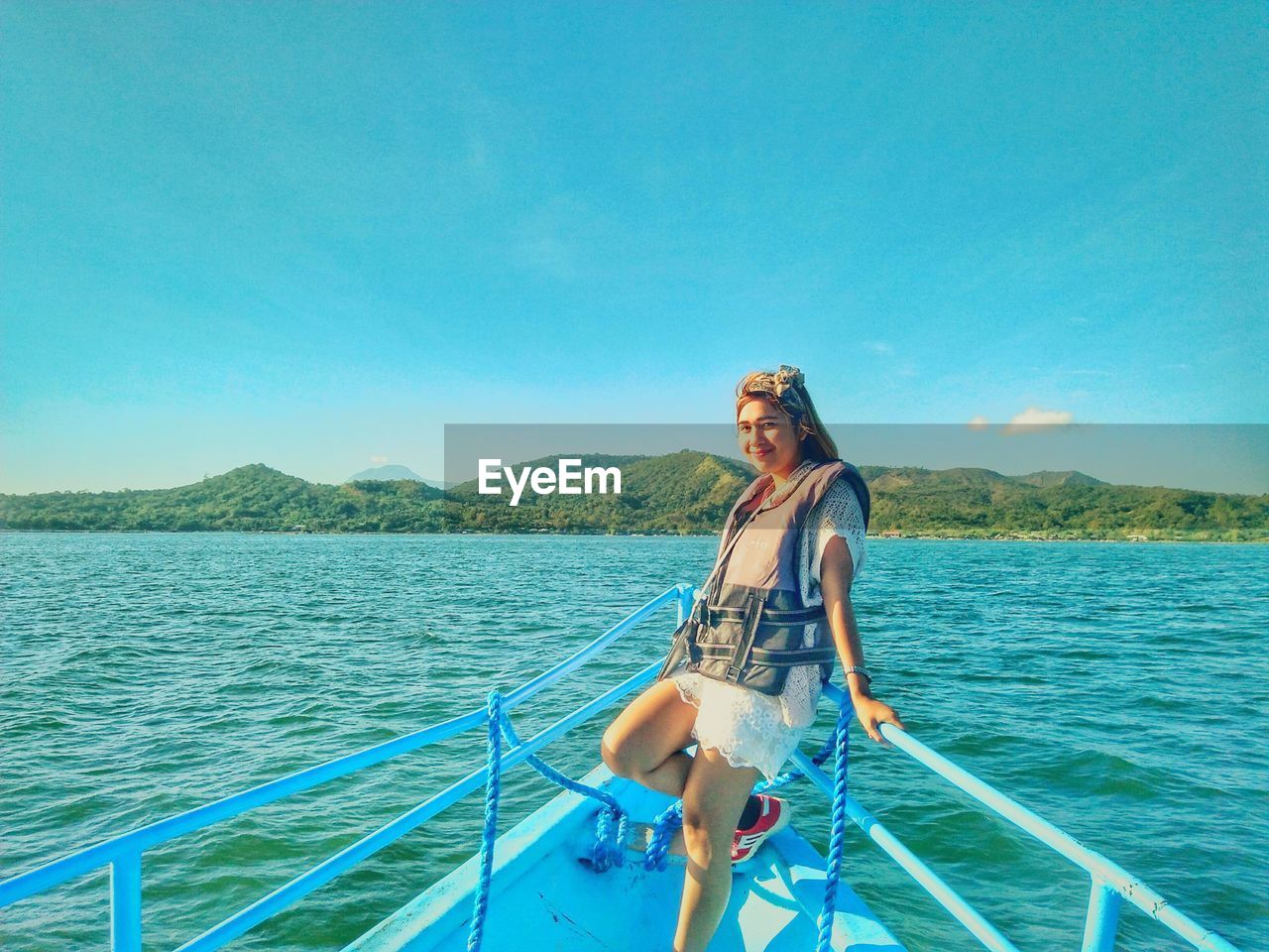 Portrait of smiling young woman in boat sailing on sea against blue sky