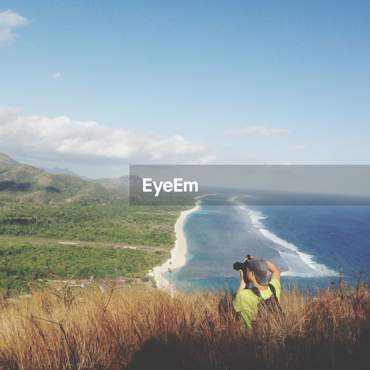 Rear view of man photographing ocean and landscape against sky