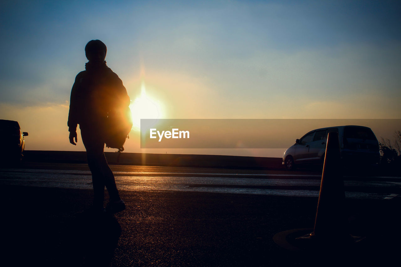 Rear view of silhouette person walking on road against sky during sunset