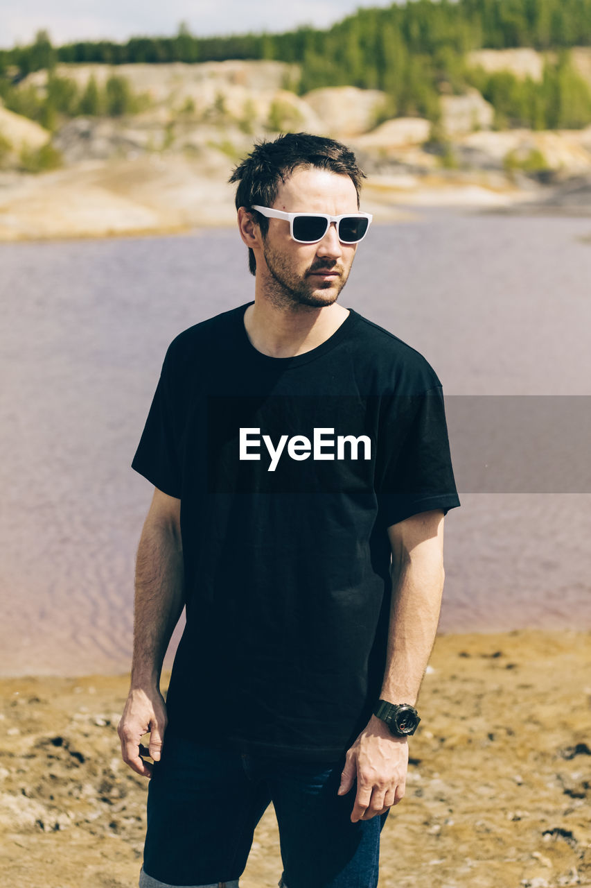 Handsome man wearing sunglasses standing against lake