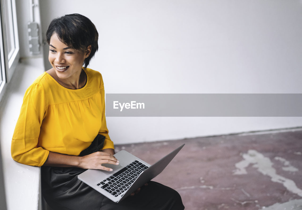 Smiling woman sitting at the window using laptop