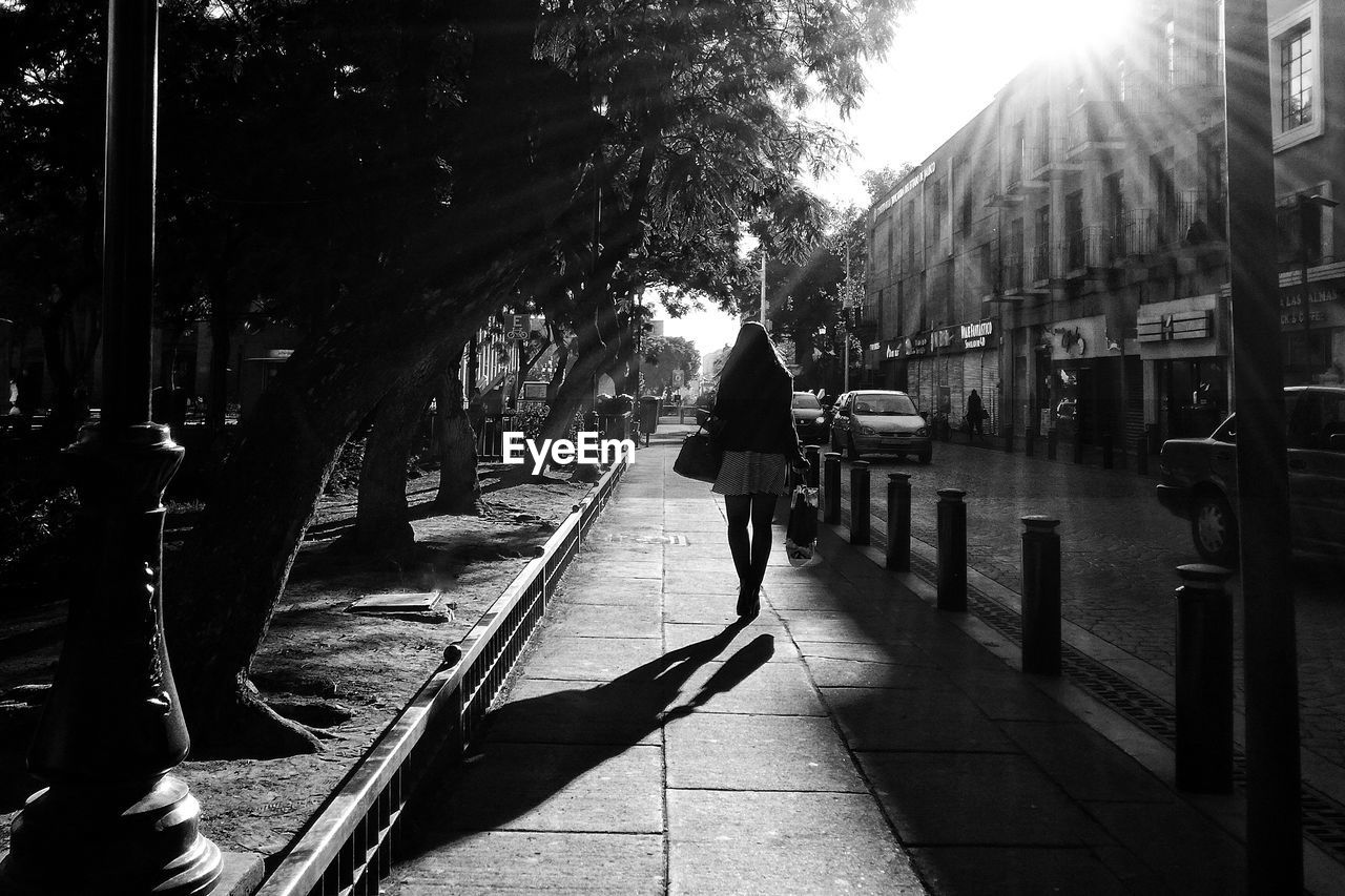 REAR VIEW OF PEOPLE WALKING ON ROAD ALONG TREES