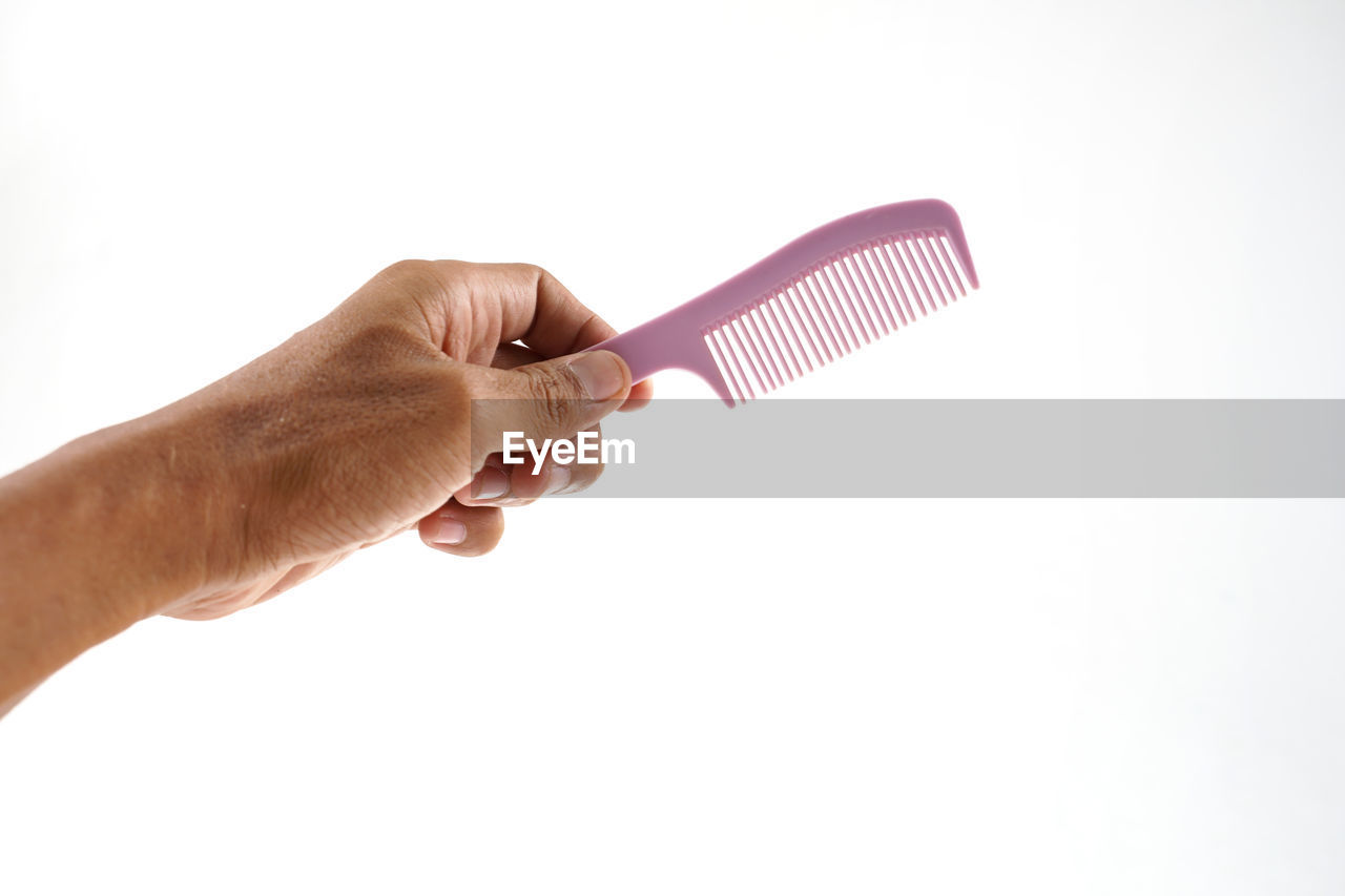 Close-up of hand holding hairbrush against white background