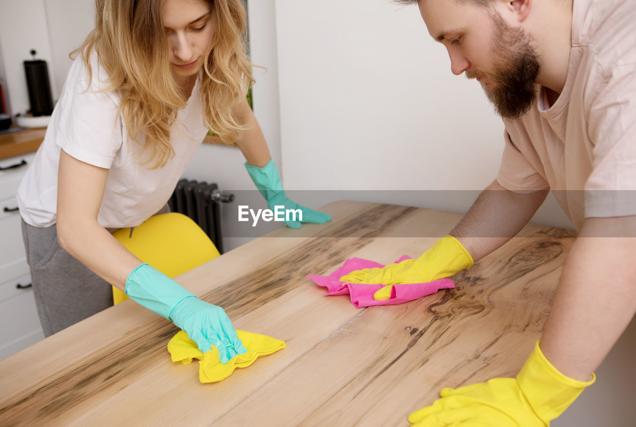 Man and woman cleaning wooden table at home