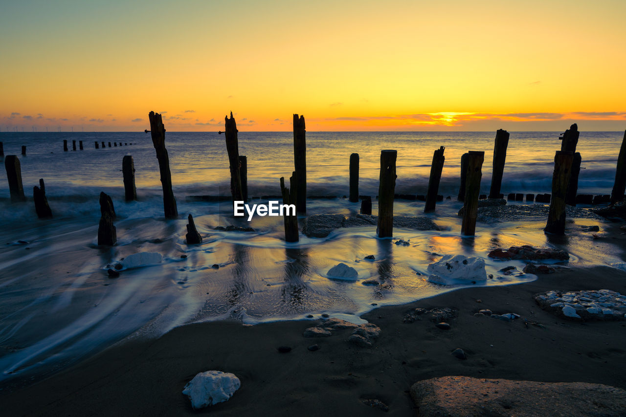 Wooden posts at beach against sky during sunset