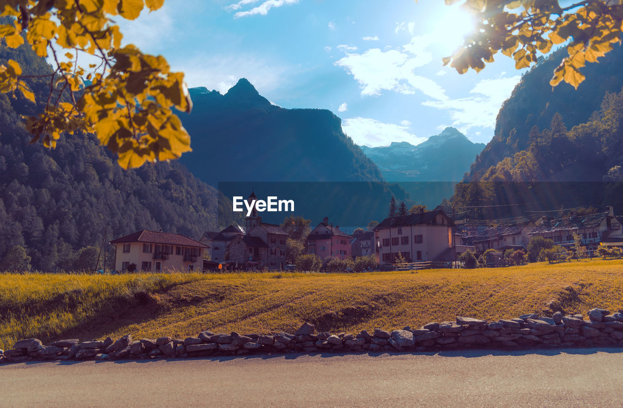 Scenic view of field by houses and mountains against sky