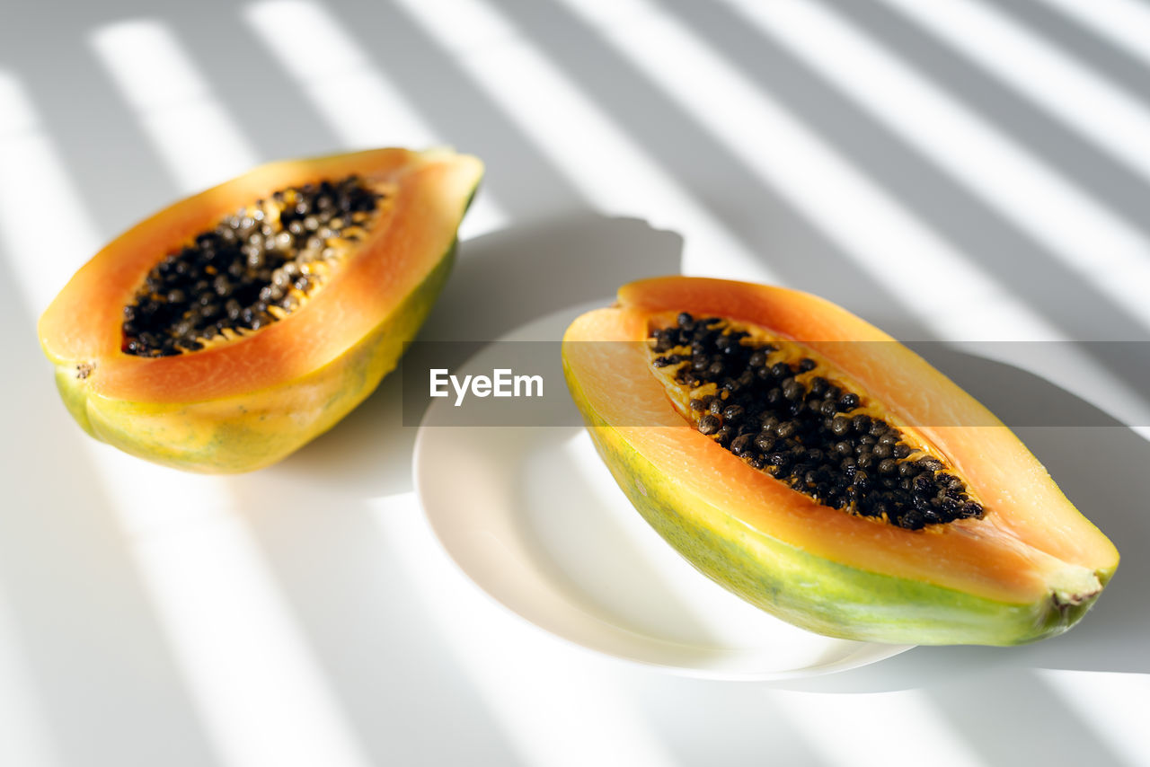 Papaya on a plate on a white table. bright sunlight through the blinds. contrasting shadows.