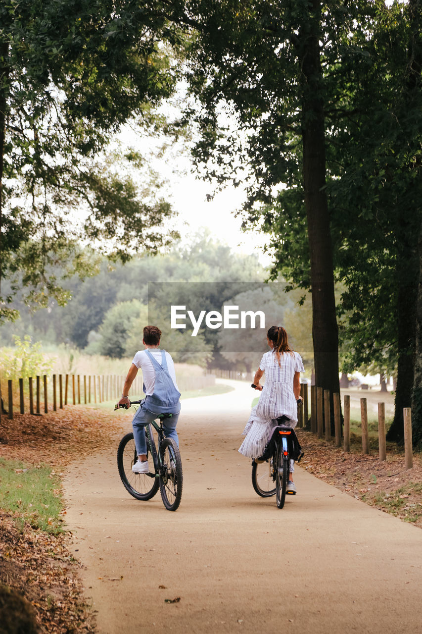 Couple riding bicycles on dirt road amidst trees