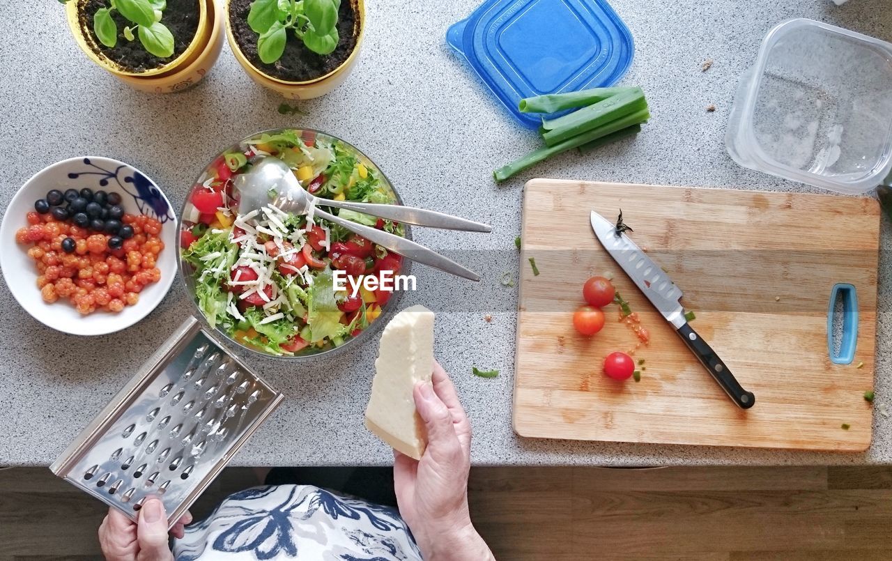 Midsection of woman holding cheese and grater by food on kitchen counter