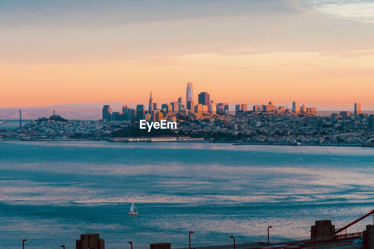 Sea and buildings against sky during sunset