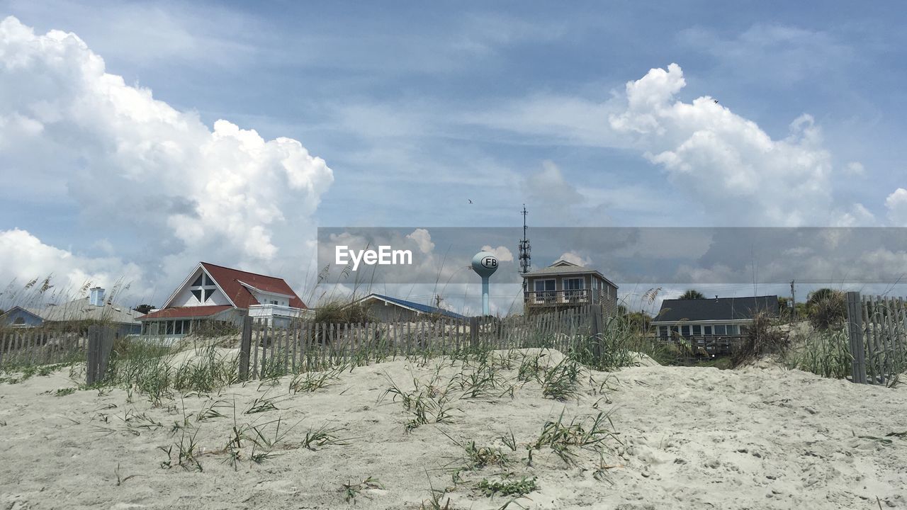 Beach by houses against cloudy sky