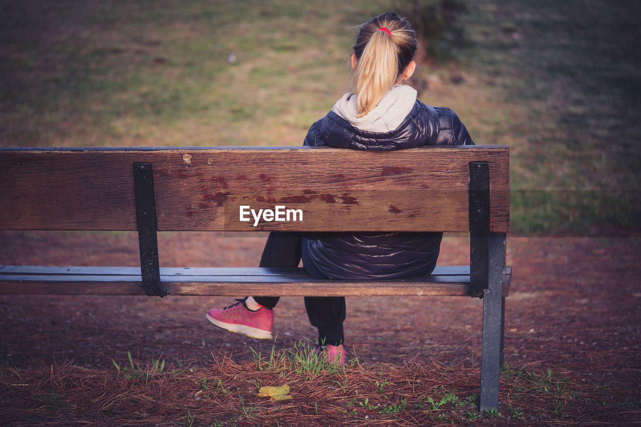 REAR VIEW OF WOMAN SITTING ON BENCH AGAINST WALL