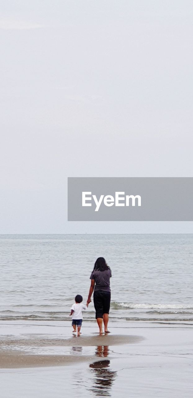 Rear view of people on sea shore against sky