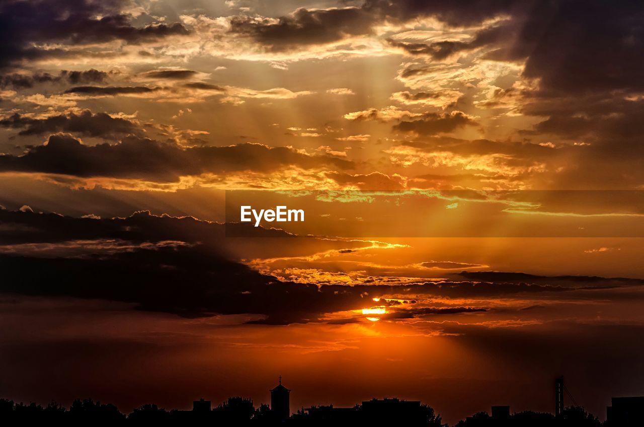 Silhouette buildings against cloudy sky at sunset