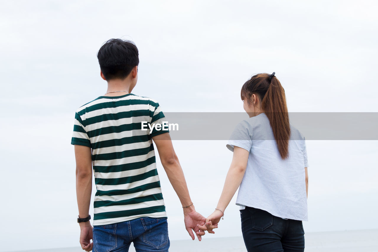 Rear view of couple holding hands against clear sky