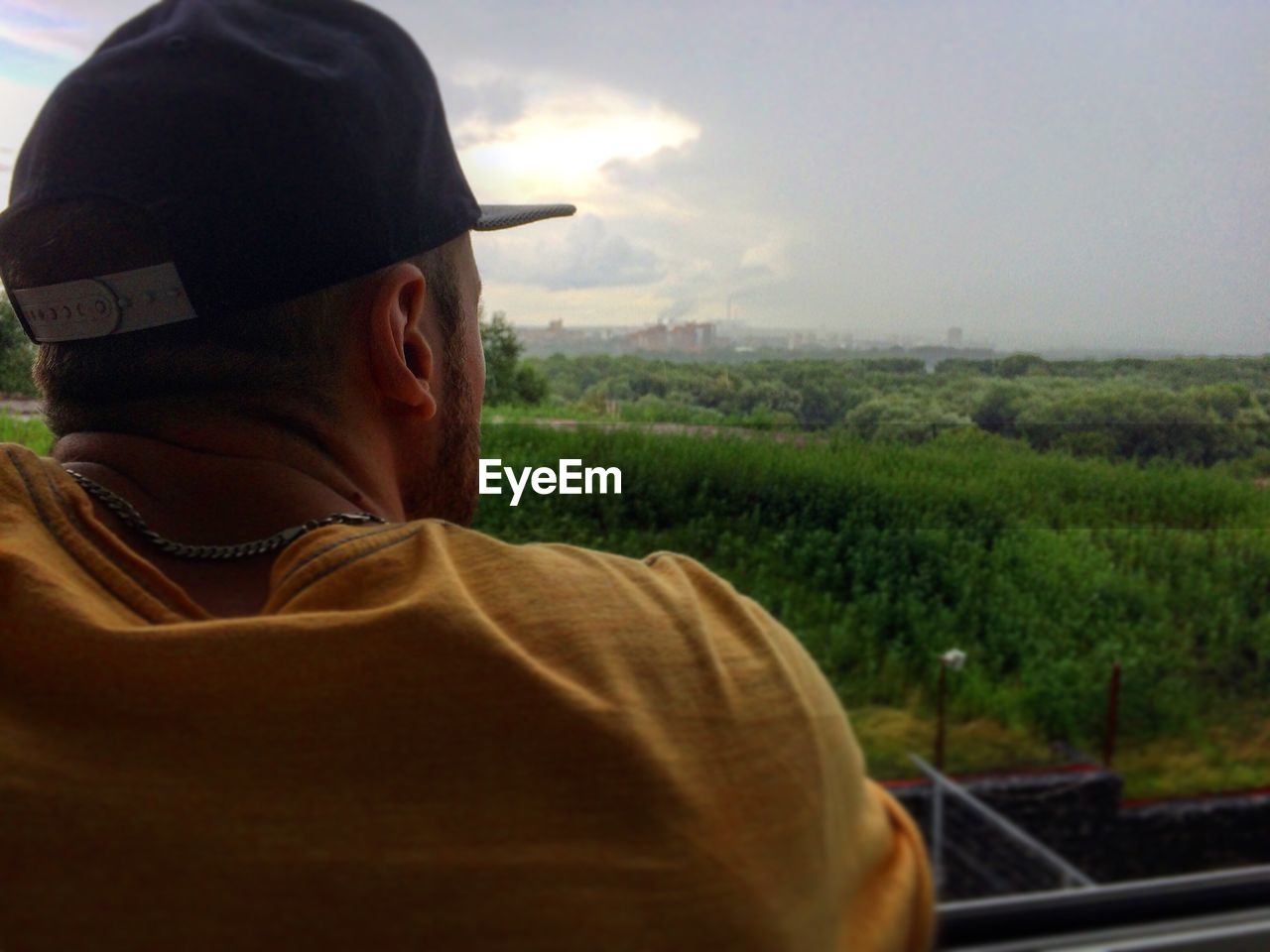 Rear view of young man wearing cap looking at view while standing by railing