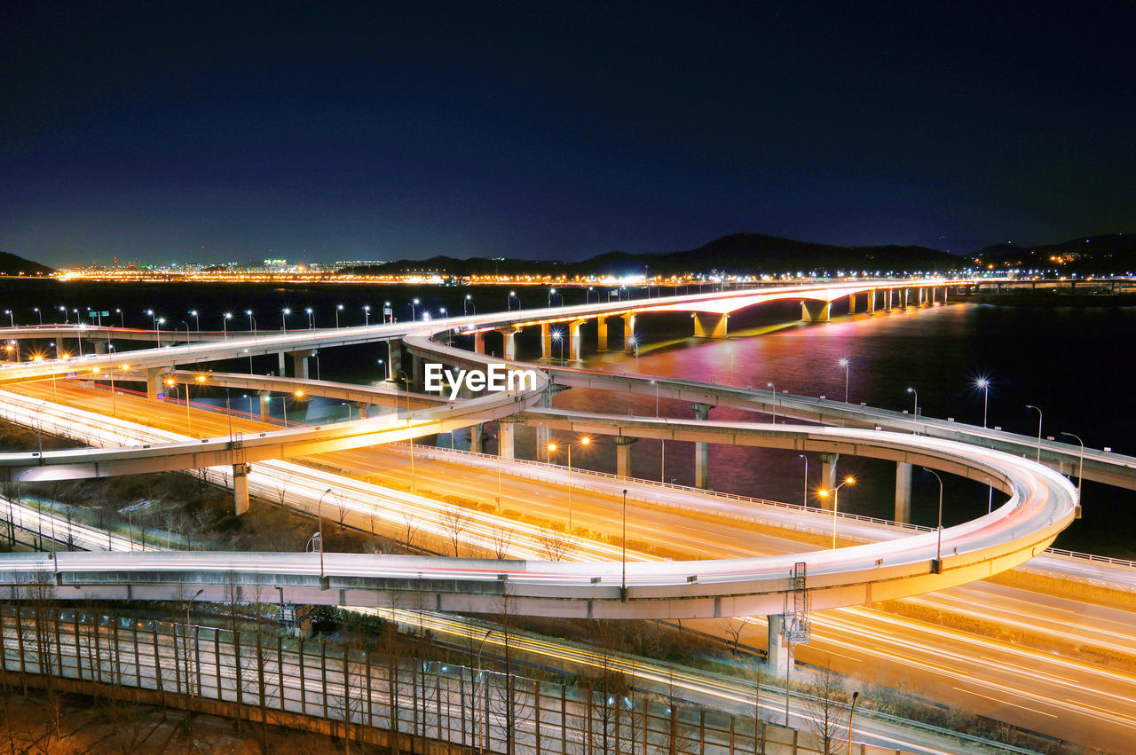 LIGHT TRAILS ON BRIDGE IN CITY AGAINST SKY