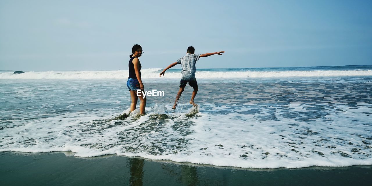 Portrait of smiling girl standing by brother jumping at beach