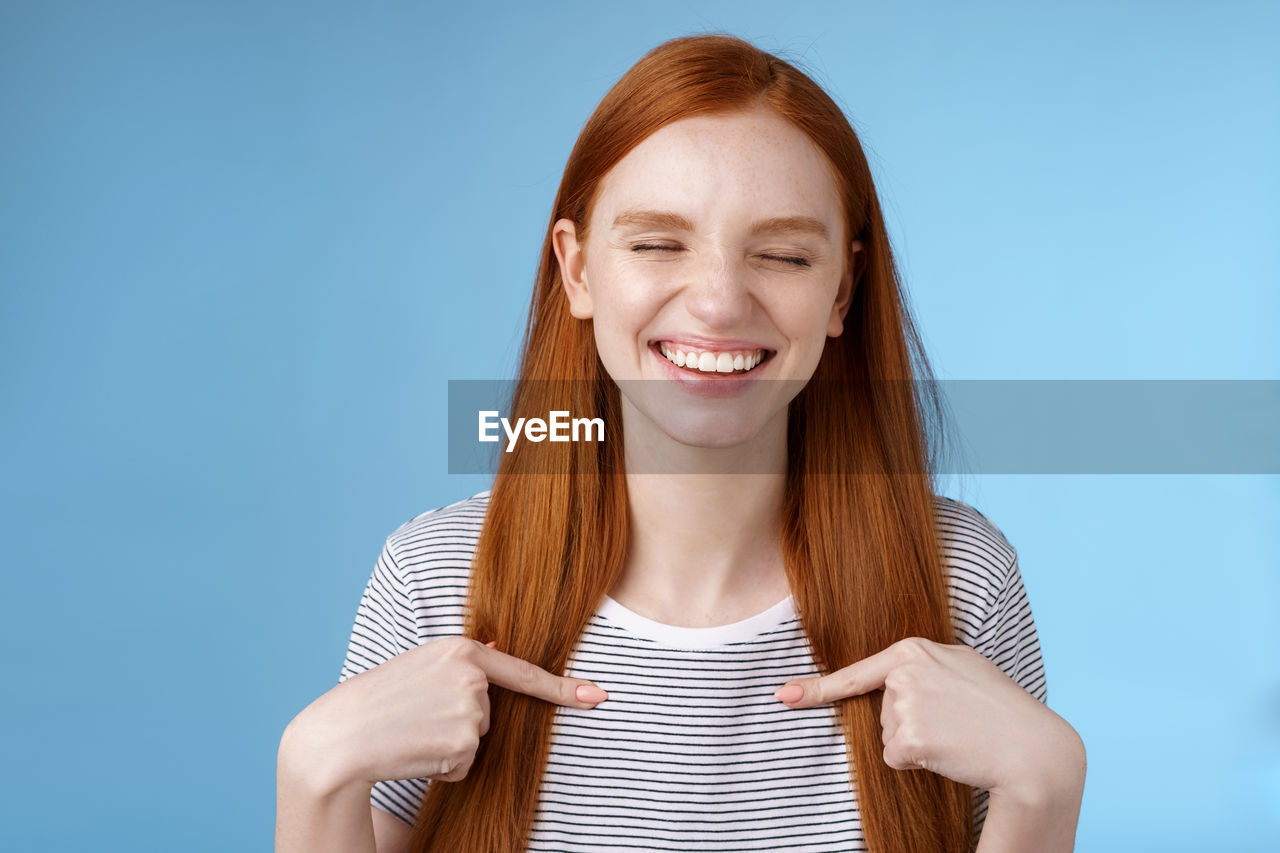 Woman pointing at self against blue background