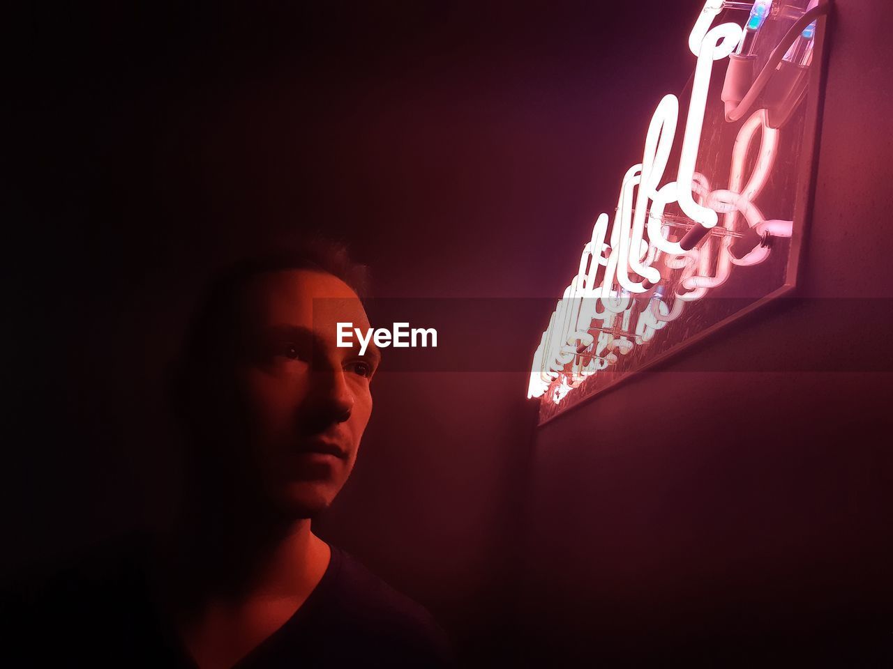 Close-up of man looking at illuminated text on wall