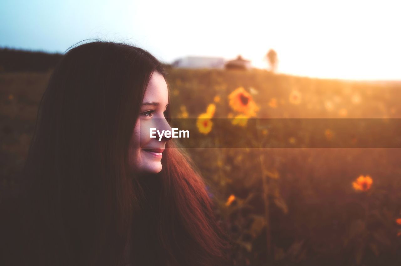 CLOSE-UP OF SMILING YOUNG WOMAN AGAINST SUNSET