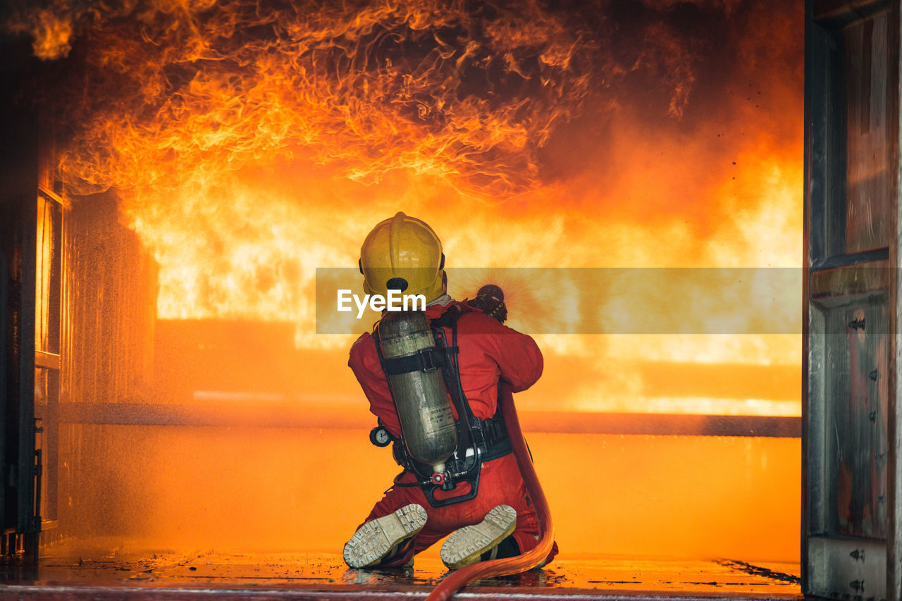 Rear view of firefighter spraying water on fire