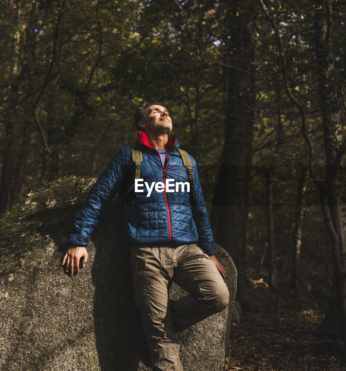 Smiling mature man leaning on rock in forest