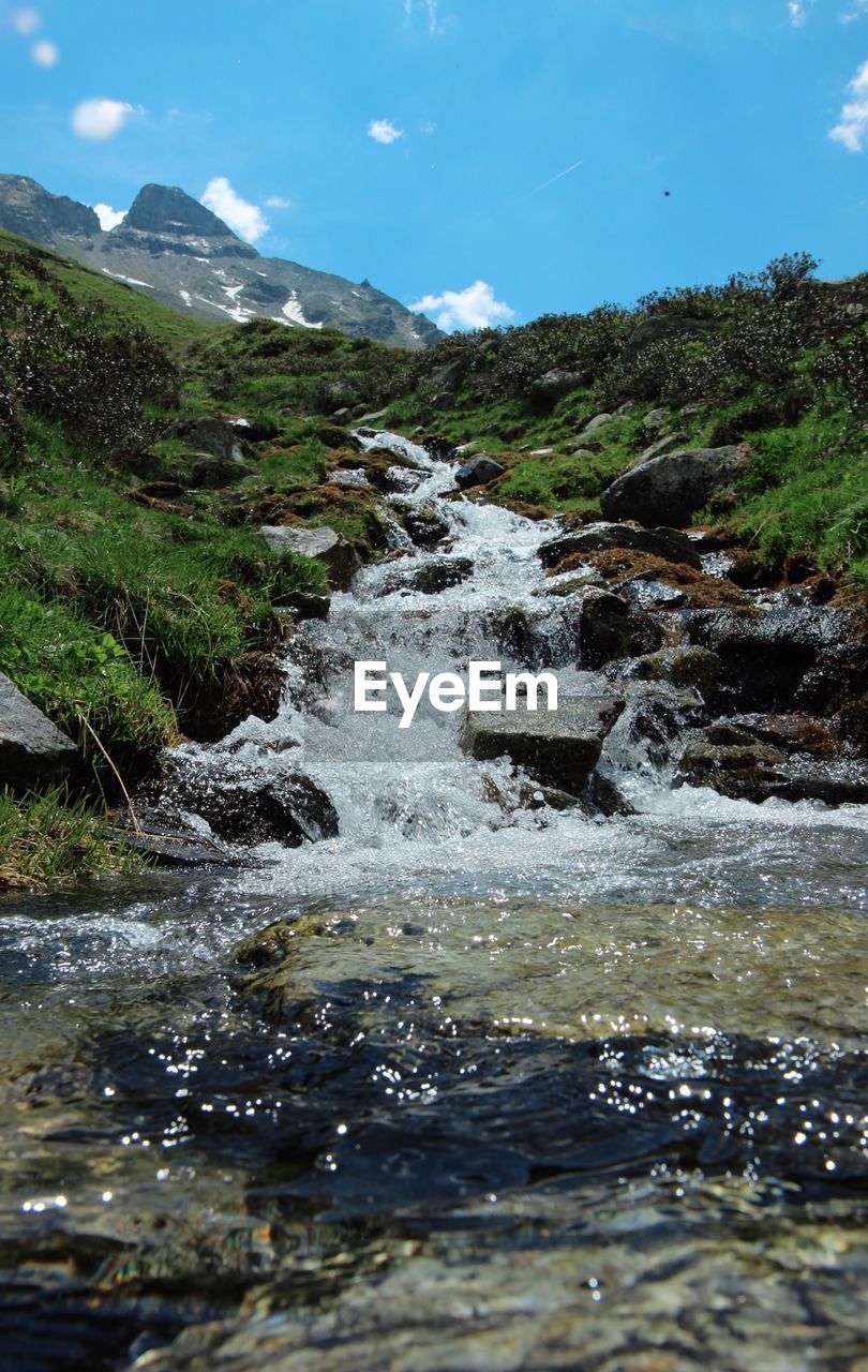 Scenic view of river flowing by mountain against sky