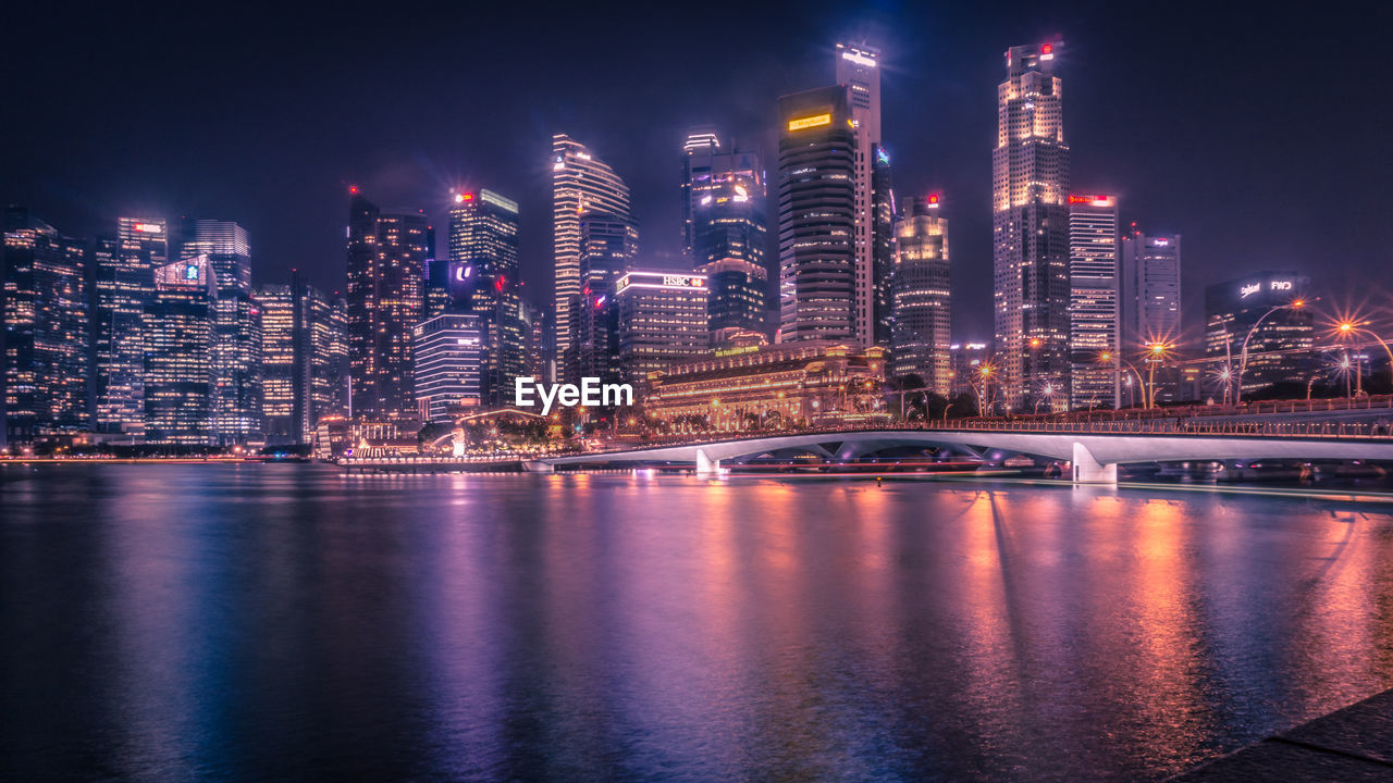 Illuminated city by buildings against sky at night