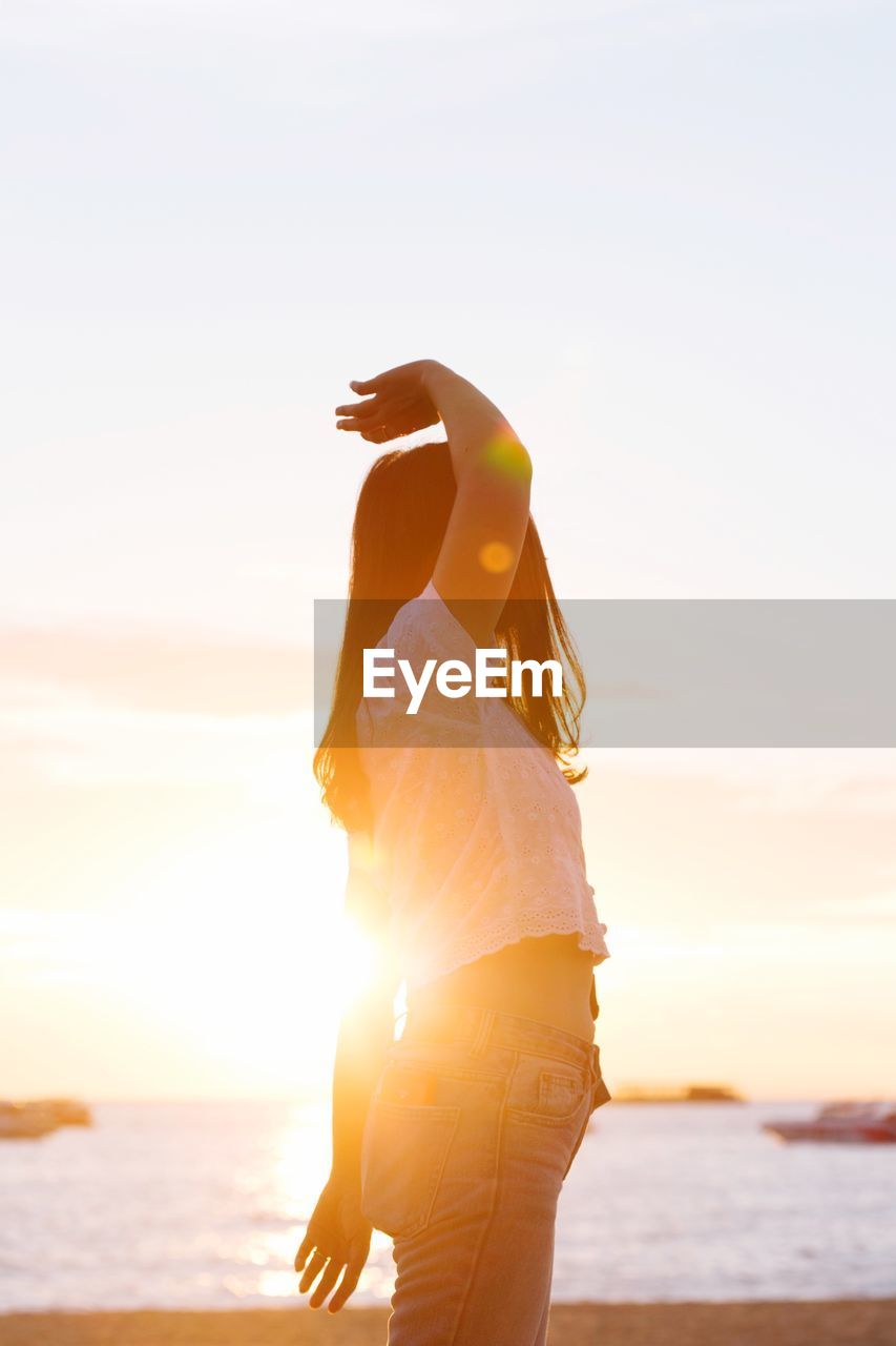 Woman standing at beach against sky during sunset