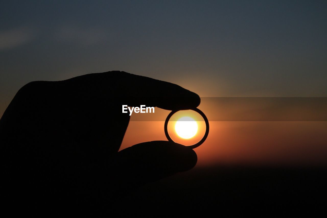 Sun seen through silhouette hand holding ring during sunset