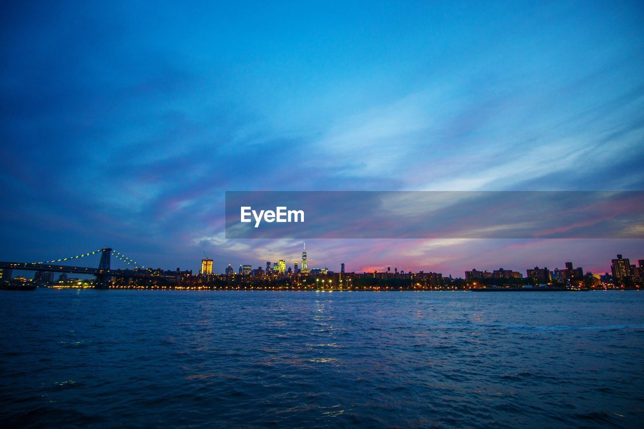 City at waterfront against cloudy sky