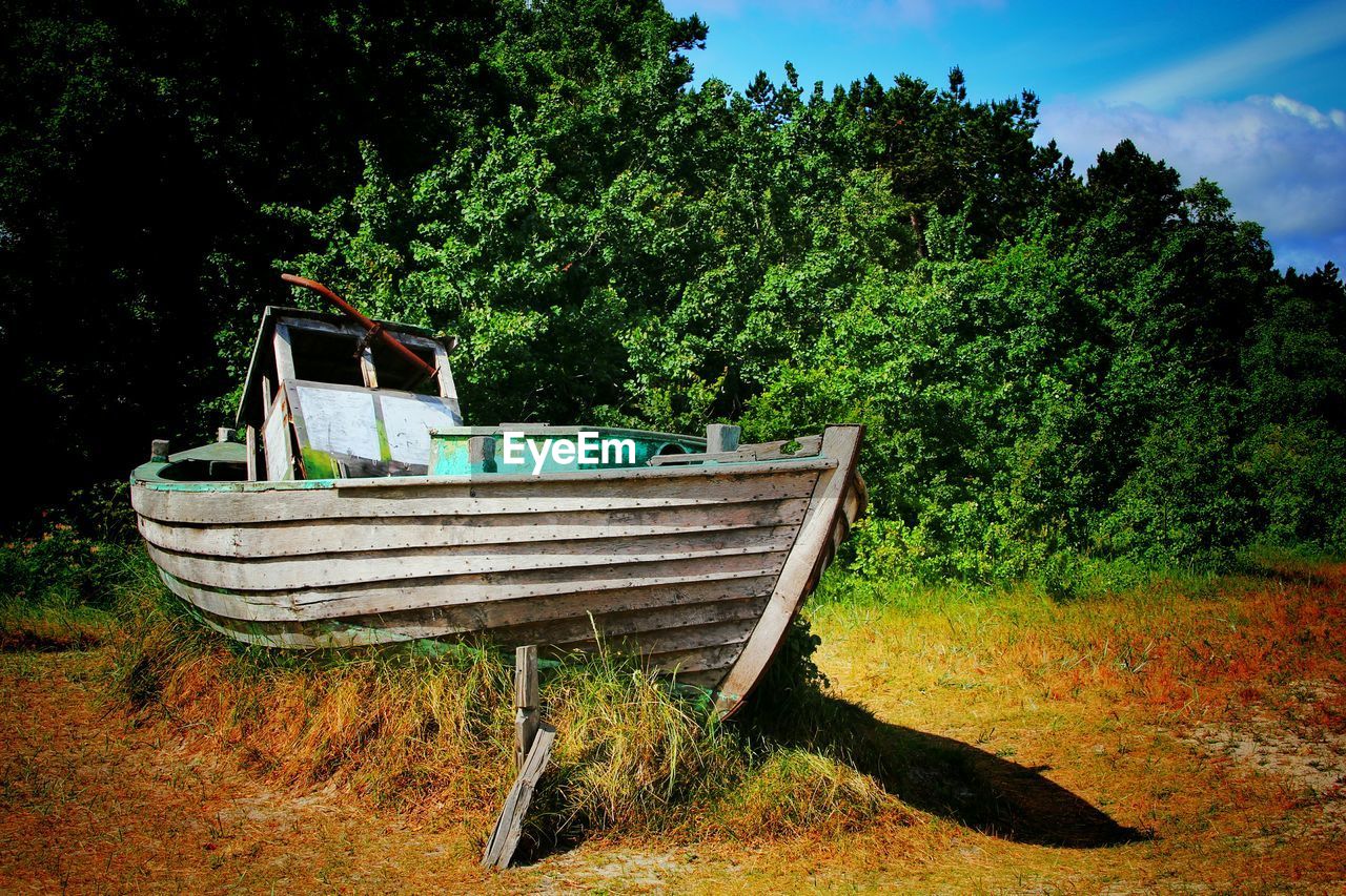 Abandoned boat moored on field by trees against sky