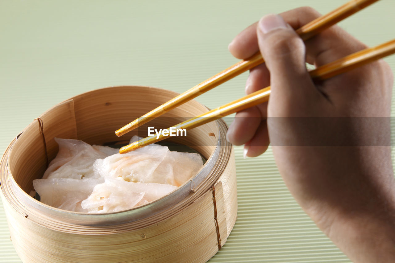 Close-up of hand having dim sum in container with chopsticks on table