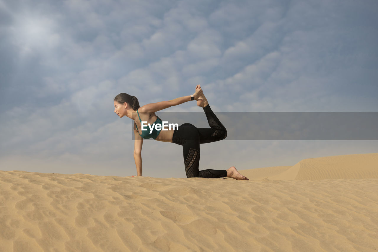 Woman exercising on sand against sky