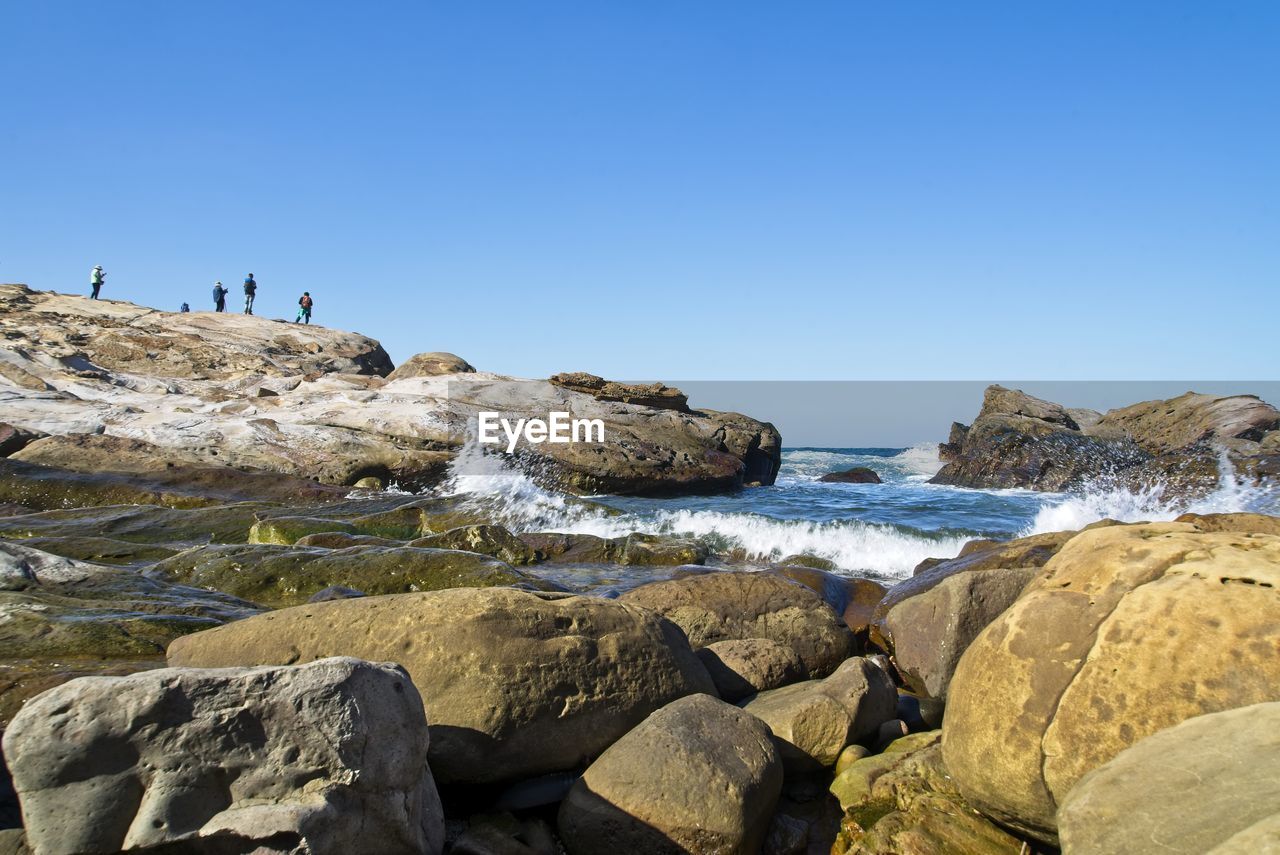 Rocks on beach against clear blue sky